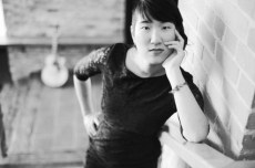 Woman seated with guitar by brick wall