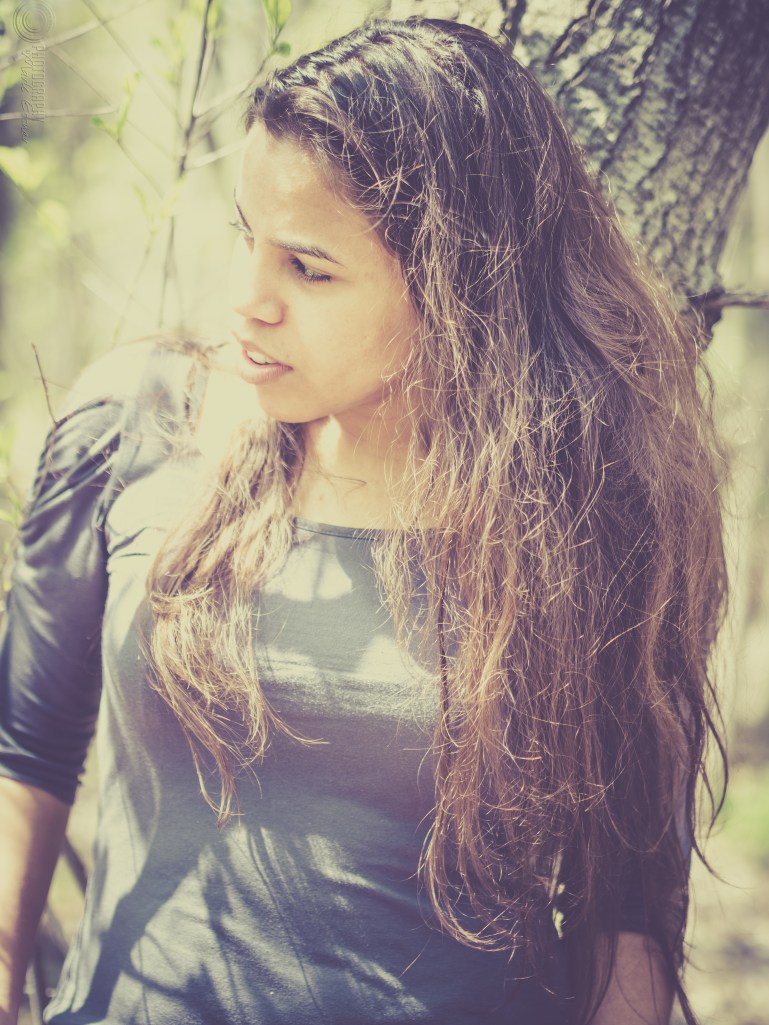 Woman in grey shirt leaning on tree