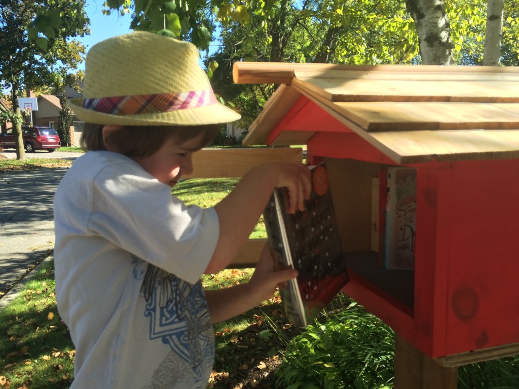 boy in hat adding books to little library